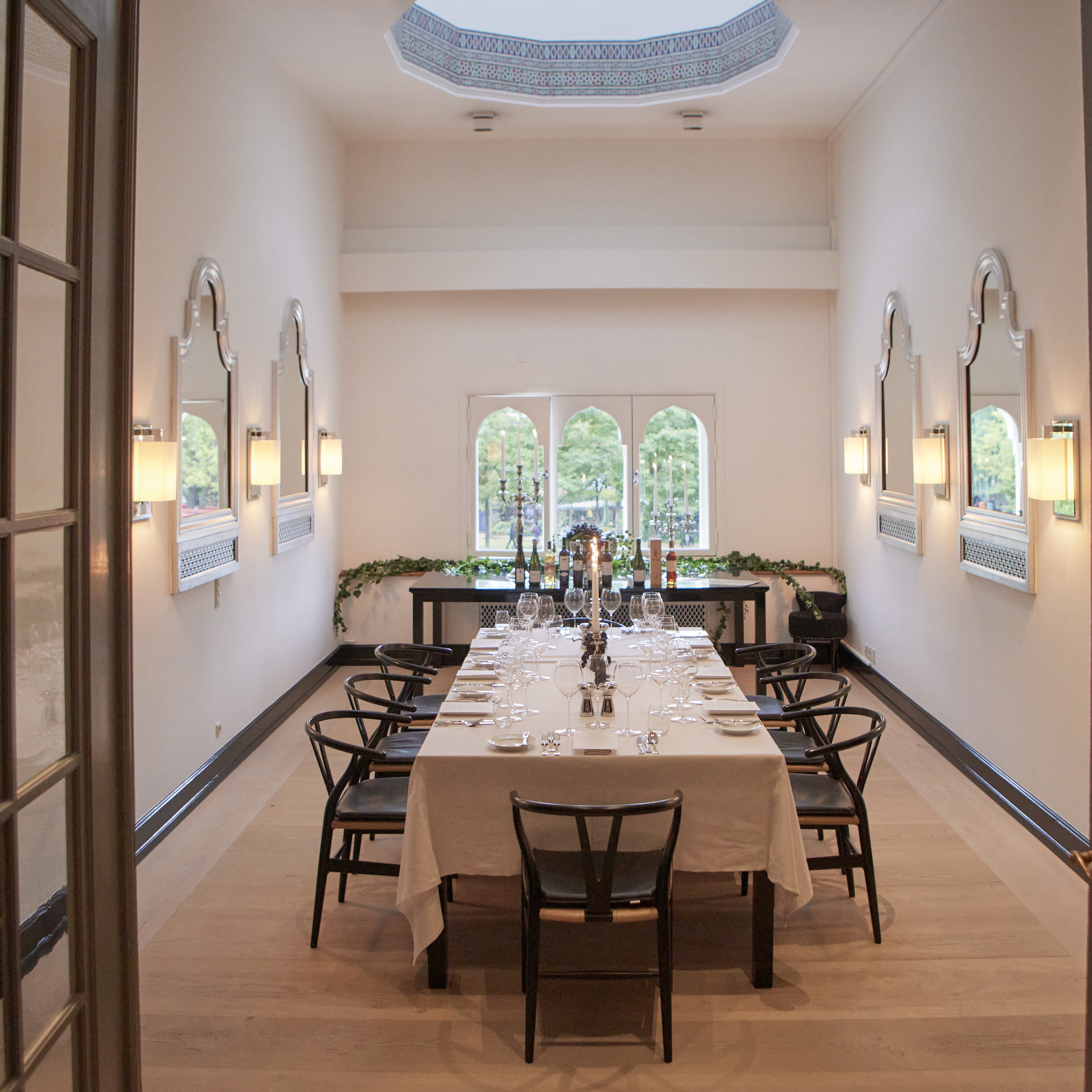 Elegant dining room with a long table set for dinner, viewed through open doors.