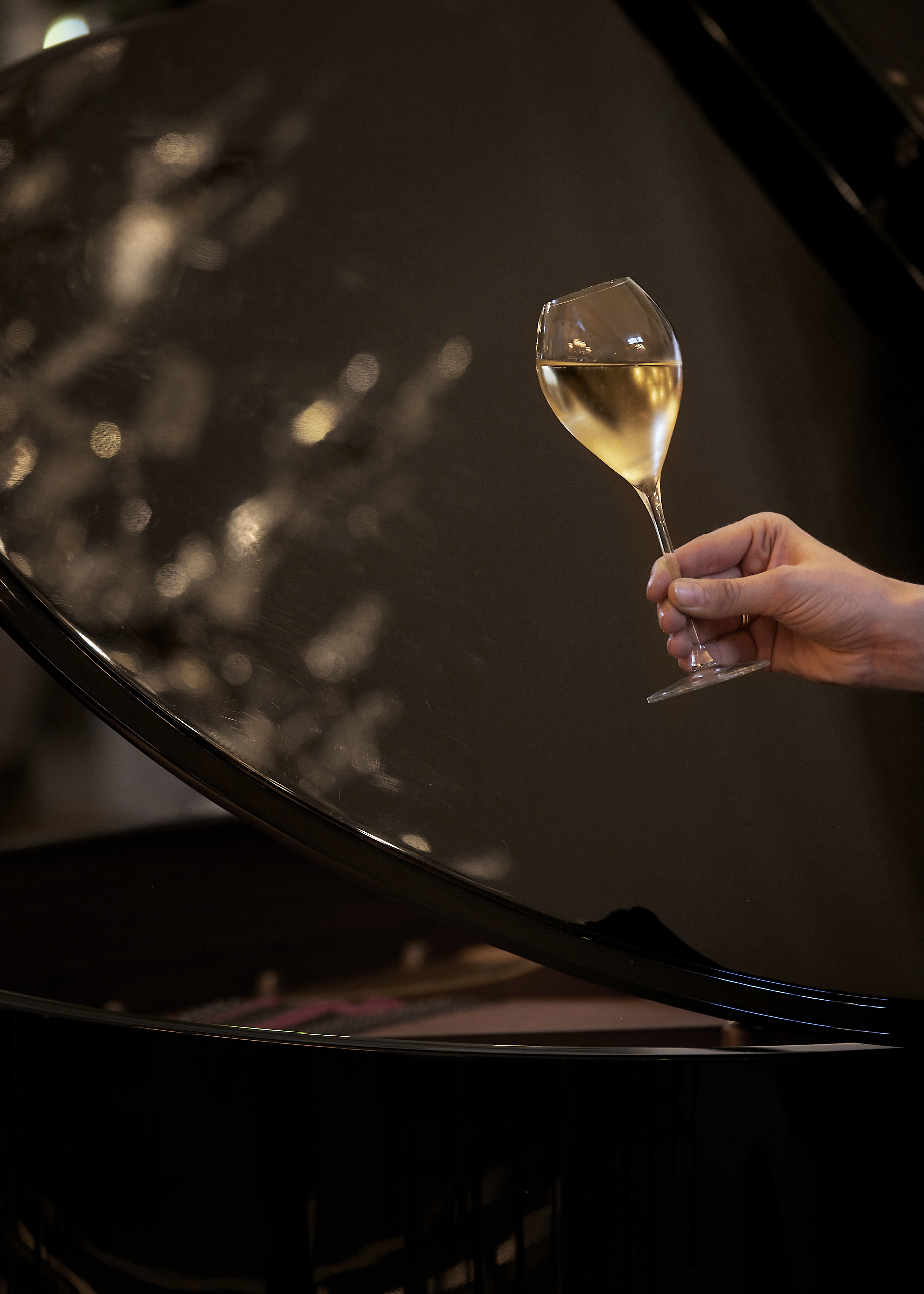 A hand holding a glass of white wine with a blurred background and light reflections.