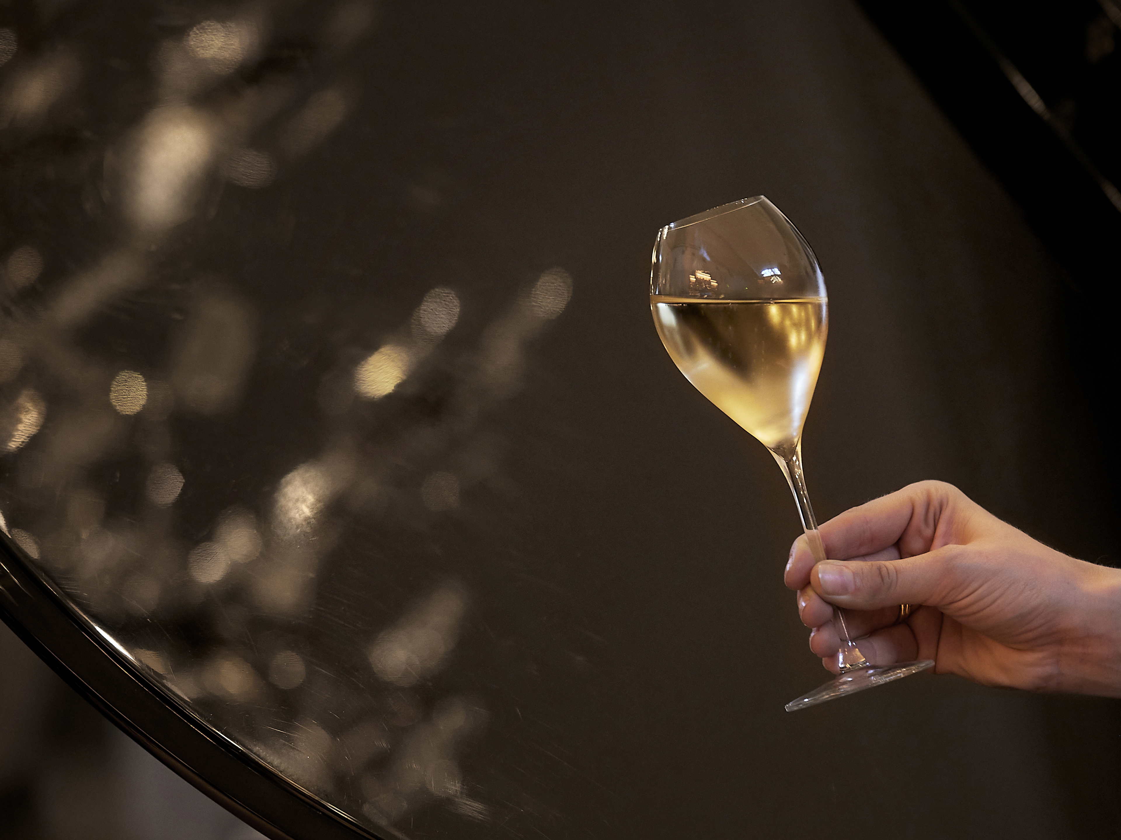 A hand holding a glass of white wine with a blurred background and light reflections.
