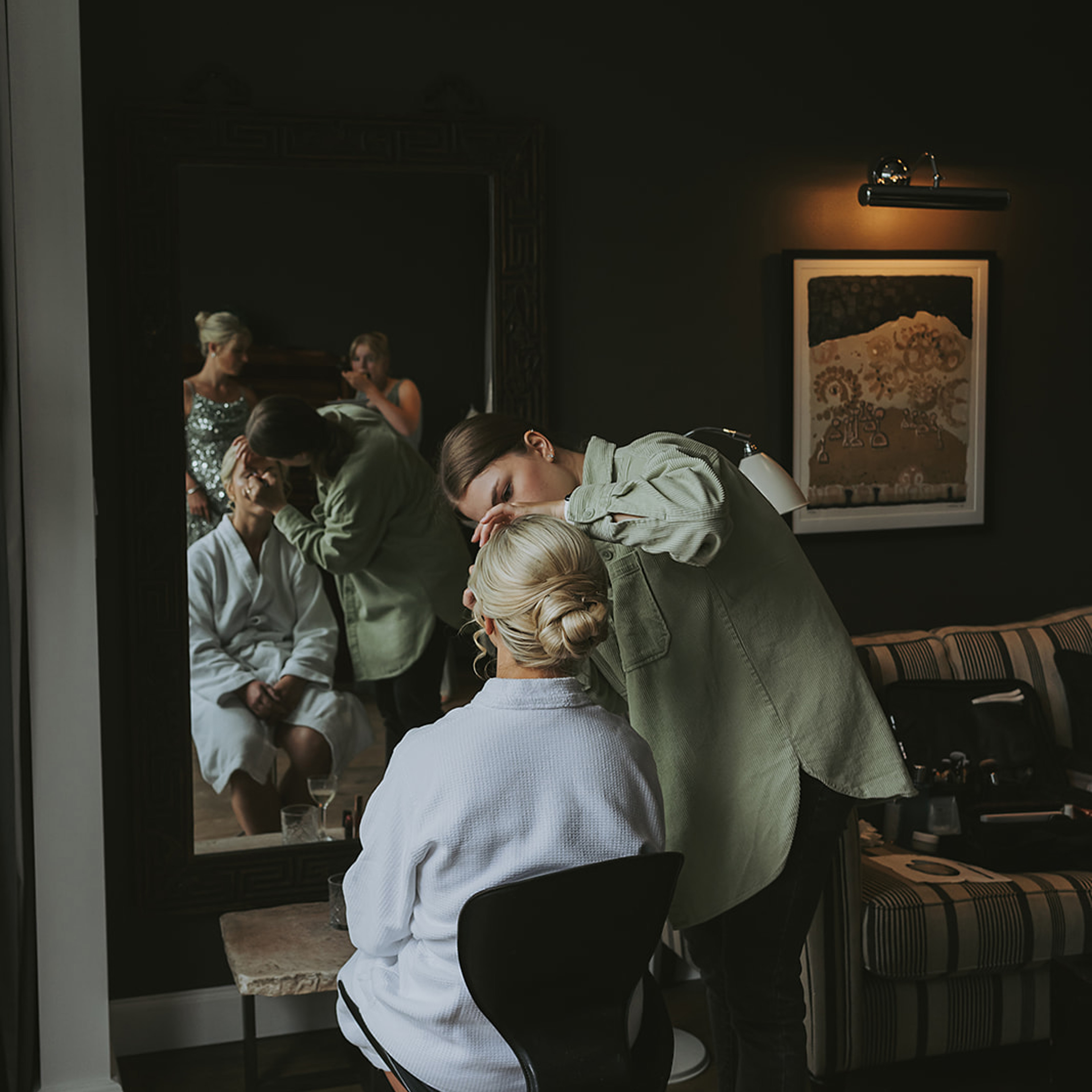 Person in white robe getting hair styled, reflected in mirror with stylist behind.